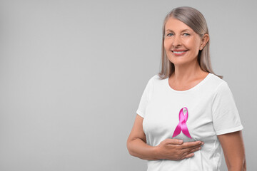 Beautiful senior woman with pink ribbon on light grey background, space for text. Breast cancer awareness - Powered by Adobe