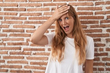 Young caucasian woman standing over bricks wall surprised with hand on head for mistake, remember error. forgot, bad memory concept.