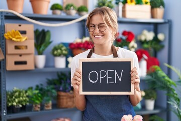 Young caucasian woman working at florist with open sign winking looking at the camera with sexy...