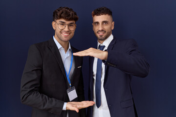 Two hispanic business men wearing business clothes gesturing with hands showing big and large size sign, measure symbol. smiling looking at the camera. measuring concept.