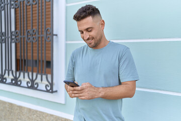 Fototapeta premium Young hispanic man smiling confident using smartphone at street