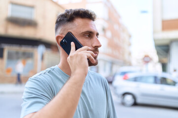 Young hispanic man talking on smartphone with serious expression at street