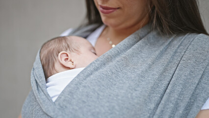Mother and baby daughter carrying baby on maternity scarf over isolated brick background