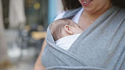 Mother and baby daughter carrying baby on maternity scarf at street