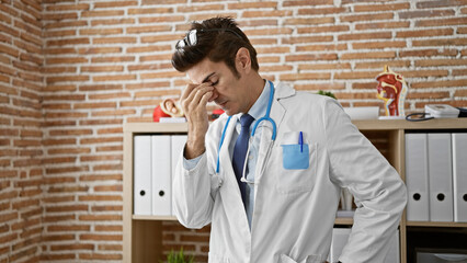 Young hispanic man doctor stressed standing at the clinic