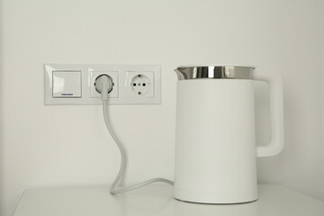 Electric kettle plugged into power socket on white wall