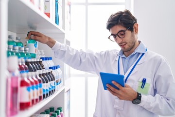 Young hispanic man pharmacist using touchpad holding medicine at pharmacy