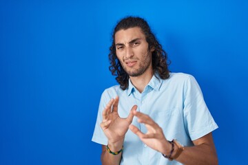 Young hispanic man standing over blue background disgusted expression, displeased and fearful doing...