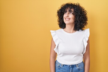 Young middle east woman standing over yellow background smiling looking to the side and staring away thinking.