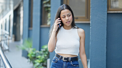 Young beautiful hispanic woman talking on smartphone with serious expression at street