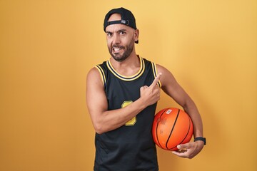 Middle age bald man holding basketball ball over yellow background pointing aside worried and nervous with forefinger, concerned and surprised expression