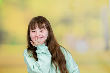 Happy teen girl with Downs syndrom stands at summer park. Empty space for text