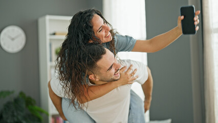 Man and woman couple holding smartphone holding girlfriend on back at home