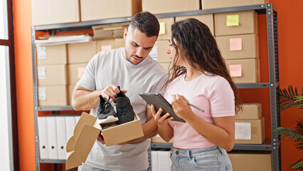 Man and woman ecommerce business workers using touchpad unpacking sneakers on cardboard box at...