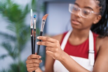 African american woman holding paintbrushes at art studio