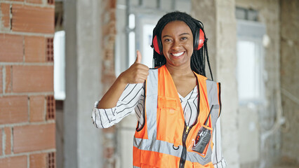 African american woman builder wearing headphones for noise doing thumb up gesture at construction site