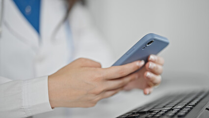 Young beautiful hispanic woman doctor using smartphone sitting on table at the clinic