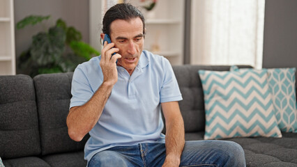 Middle age man talking on smartphone sitting on sofa at home
