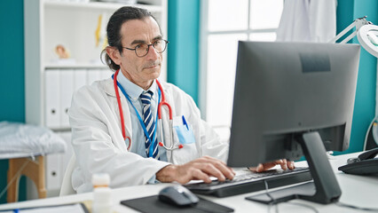 Naklejka na ściany i meble Middle age man doctor using computer at the clinic