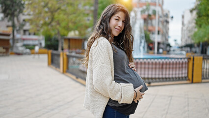 Young pregnant woman smiling confident touching belly at park