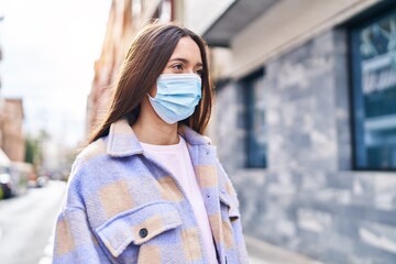 Young beautiful hispanic woman wearing medical mask standing at street