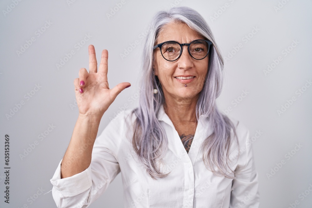 Wall mural middle age woman with tattoos wearing glasses standing over white background showing and pointing up