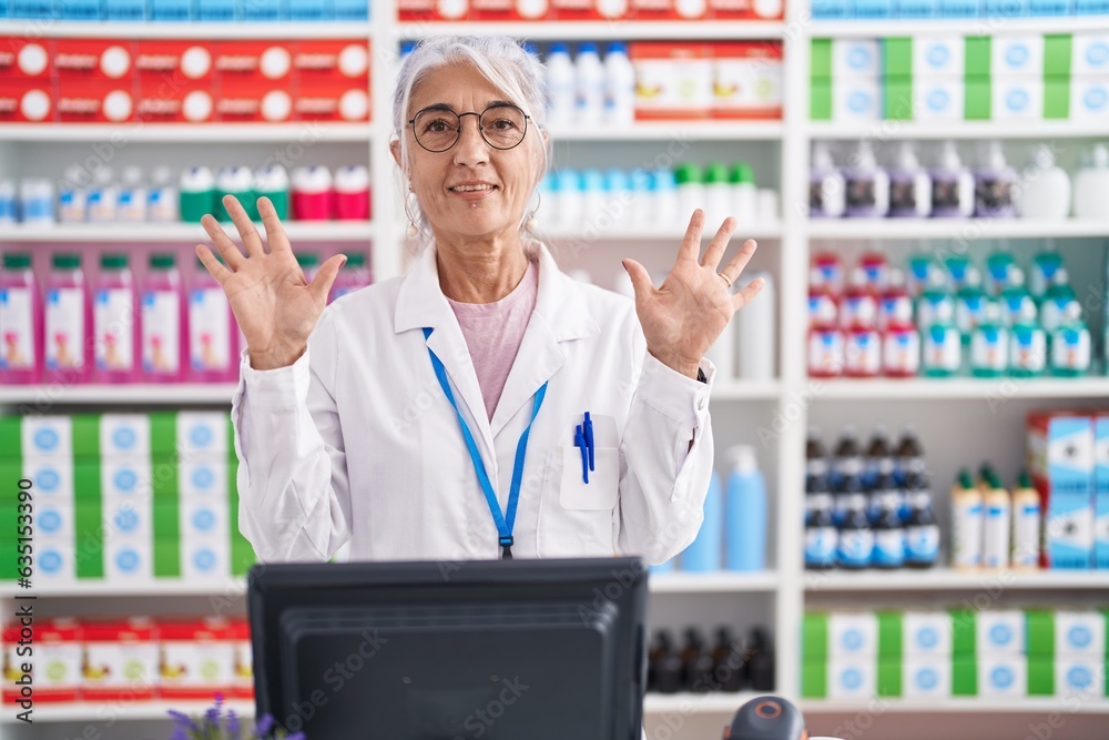 Wall mural middle age woman with tattoos working at pharmacy drugstore showing and pointing up with fingers num