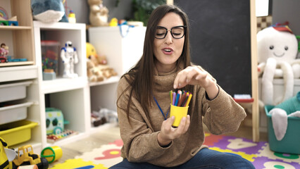 Beautiful hispanic woman preschool teacher smiling confident teaching color at kindergarten