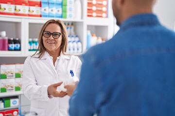 Man and woman pharmacist smiling confident holding pills bottle at pharmacy