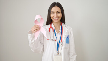 Young beautiful hispanic woman doctor holding breast cancer awareness pink ribbon over isolated...