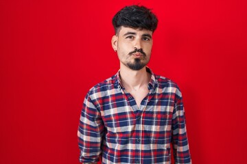 Young hispanic man with beard standing over red background looking at the camera blowing a kiss on air being lovely and sexy. love expression.
