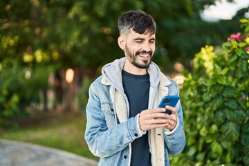 Fototapeta premium Young hispanic man smiling confident using smartphone at park