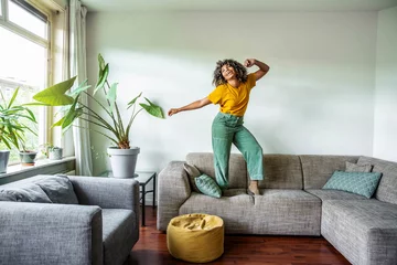 Foto op Plexiglas Happy afro american woman dancing on the sofa at home - Smiling girl enjoying day off lying on the couch - Healthy life style, good vibes people and new home concept © Davide Angelini