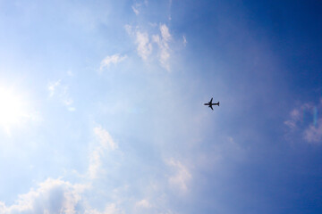 Naklejka na ściany i meble Low-angle shot of an airplane flying under a cloudy blue sky. Symmetrical airplane silhouette photography