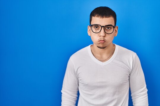 Young arab man wearing casual white shirt and glasses puffing cheeks with funny face. mouth inflated with air, crazy expression.