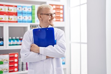 Naklejka na ściany i meble Young caucasian man pharmacist smiling confident holding clipboard at pharmacy