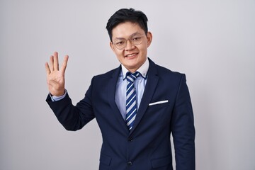 Young asian man wearing business suit and tie showing and pointing up with fingers number four while smiling confident and happy.