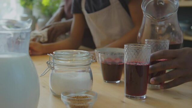 Cropped shot of unrecognizable African American man pouring red Zobo tea into glasses while cooking traditional food with family in kitchen at home