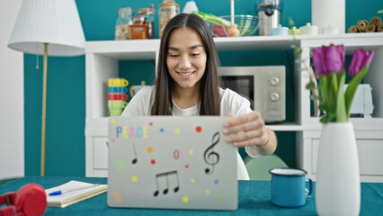 Young beautiful hispanic woman using laptop sitting on table at dinning room