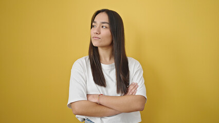 Obraz premium Young beautiful hispanic woman standing with serious expression and arms crossed gesture over isolated yellow background
