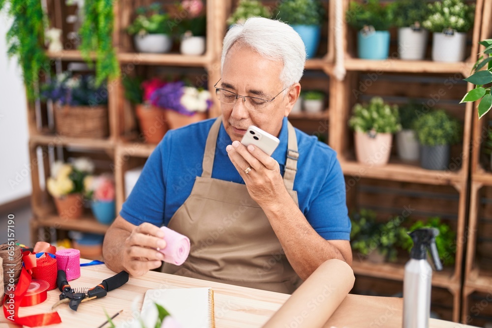 Sticker Middle age grey-haired man florist talking on smartphone holding gift lace at florist