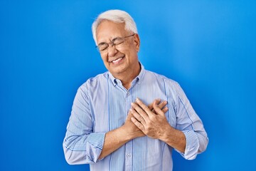 Hispanic senior man wearing glasses smiling with hands on chest with closed eyes and grateful gesture on face. health concept.