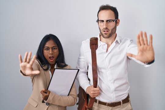 Interracial business couple wearing glasses doing stop gesture with hands palms, angry and frustration expression