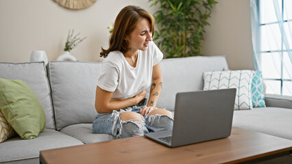 Young woman using laptop sitting on sofa suffering for stomachache at home