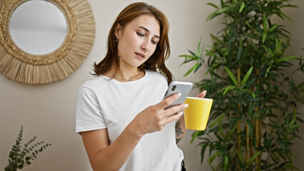 Young woman holding cup of coffee using smartphone at home