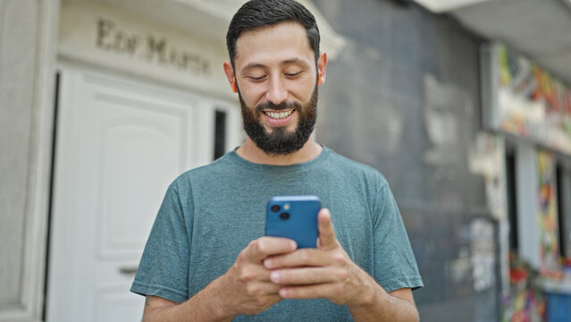 Young hispanic man using smartphone and earphones smiling at street