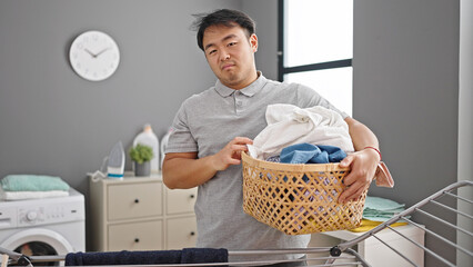  holding basket with clothes with serious expression at laundry room