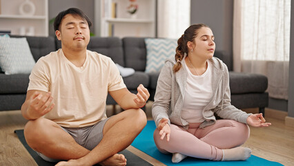 Fototapeta na wymiar Man and woman couple sitting on floor doing yoga exercise at home