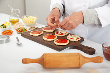 Obraz na płótnie Canvas Adding toppings to the mini pizzas. Adding cheese. Delicious homemade mini pizzas preparation.