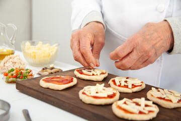 Obraz na płótnie Canvas Adding toppings to the mini pizzas. Adding cheese. Delicious homemade mini pizzas preparation.